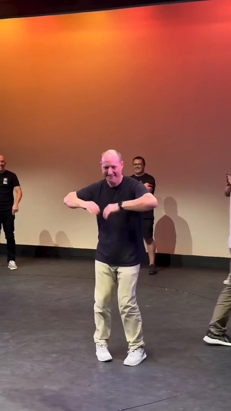 A grinning dad doing the chicken dance on stage at the Dance Dad Battle