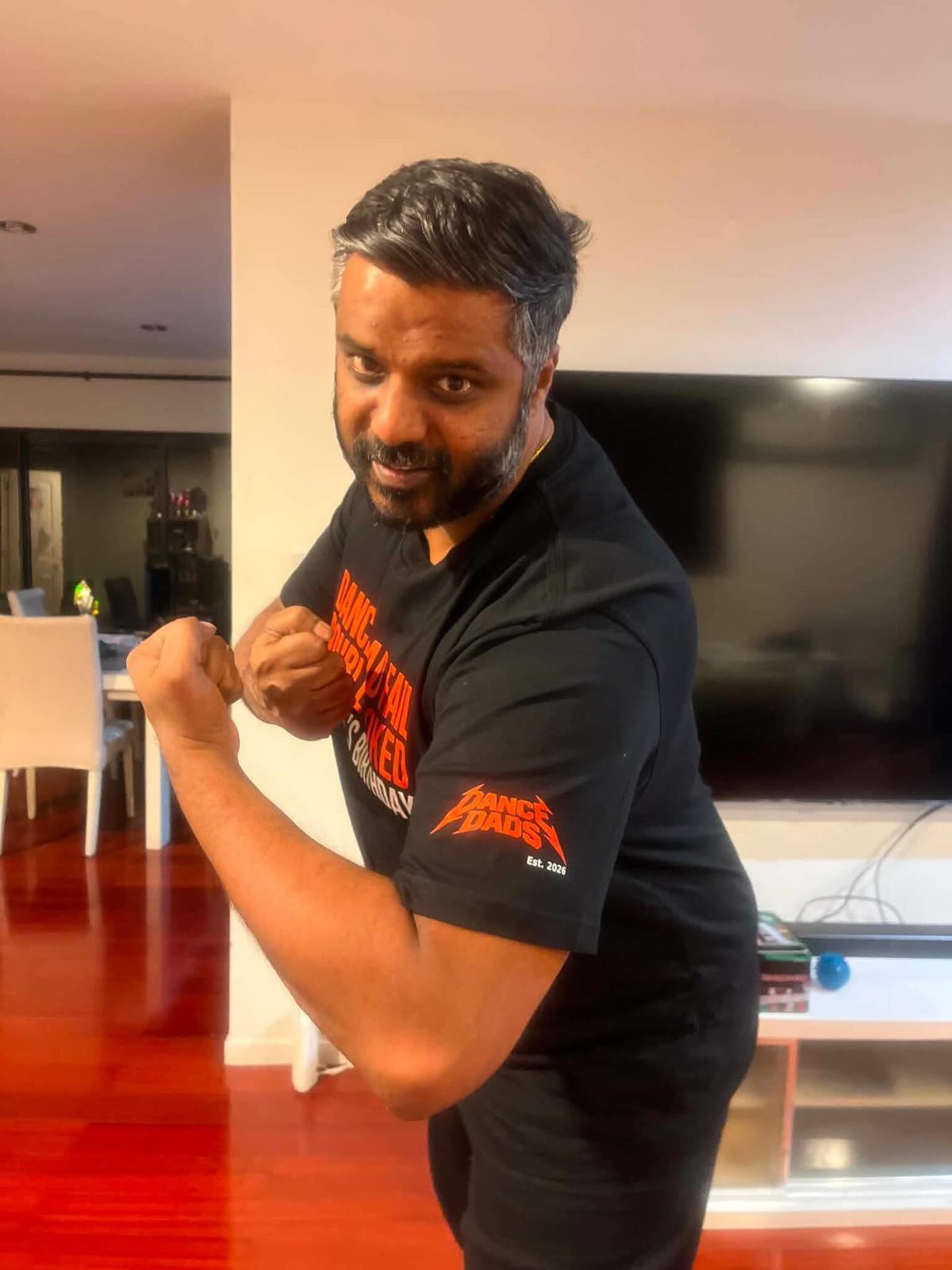 Our first customer doing the Van Damme pose, fists up, in his custom black Dance Dads tee with the orange Dance Dads logo on the sleeve