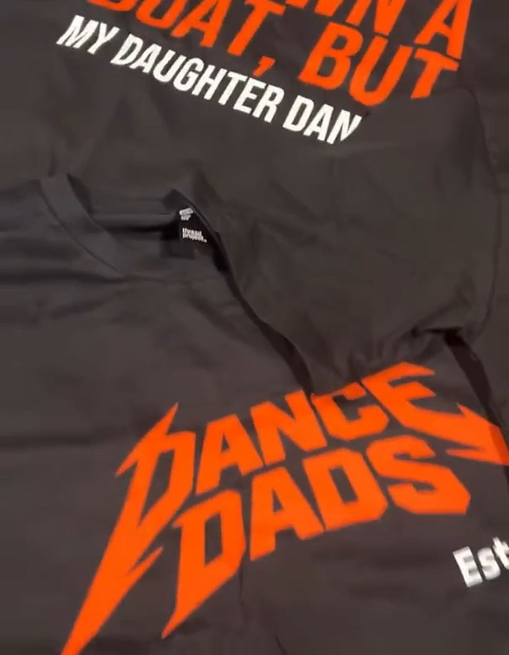 Real printed tees on a table: the I'd Own A Boat tee next to the OG Tee