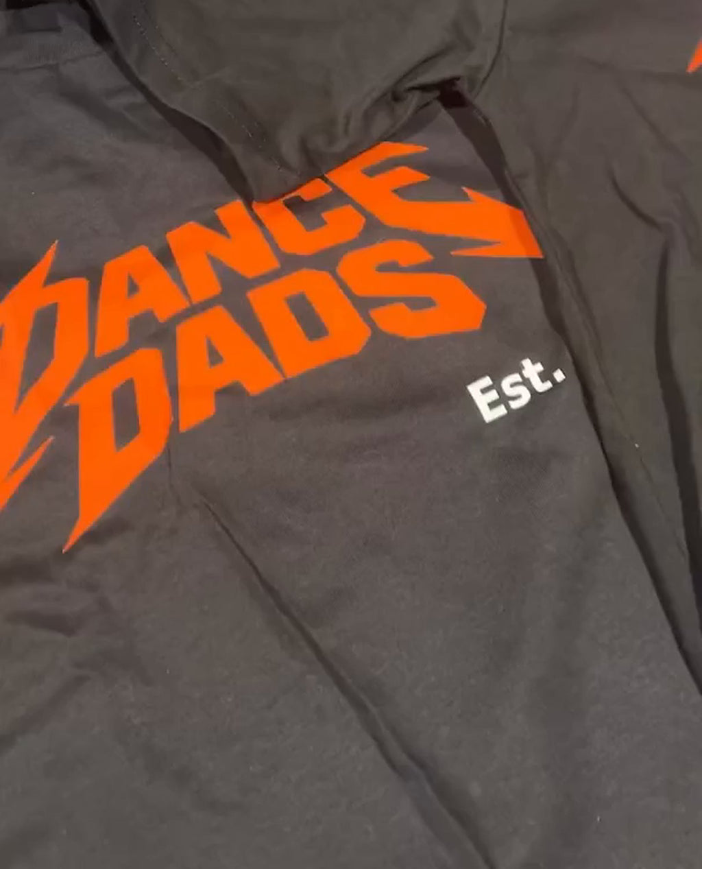 Close-up of a real OG Tee: the burnt-orange Dance Dads print on black cotton